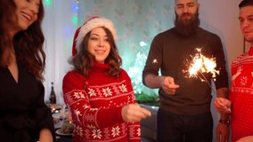 Friends celebrate Christmas at home party. Group of people 4 people with sparklers celebrates the new year 2022. Happy emotional women and men in santa hats. Celebration, holidays 4k footage. 