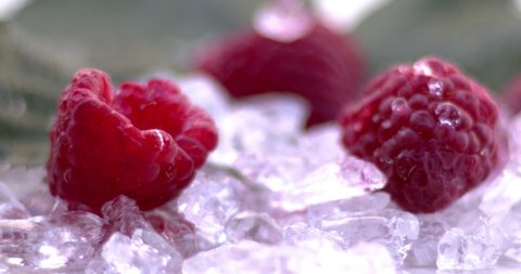 Raspberries on cold ice. A drop of water falls on the raspberry. Natural cold fruits, juicy and aromatic food.  Slow motion, 8K downscale. 4K.