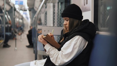Talented artistic female drawing painting in metro using sketchbook and pencil. Young relaxed female artist drawing while traveling in metro subway tube underground 