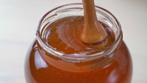 Wooden spoon mixes honey in the jar. Golden organic honey dripping in a bowl with a wooden stick closeup. Concept of healthy nutrition organic food. Background for beekeepers, healthy food stores