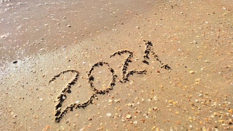 The inscription 2021 on the sand is erased by the sea wave. Happy new year 2022 concept