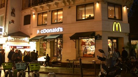 PARIS, FRANCE - 30 OCTOBER 2021: McDonald's Restaurant Frontage in Centre of Paris at Night Lights, people walk i