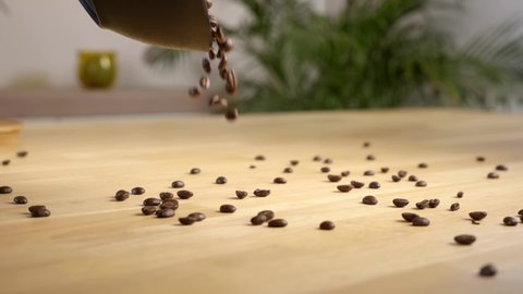 Mouthwatering dark roasted coffee beans pouring onto a light wooden surface