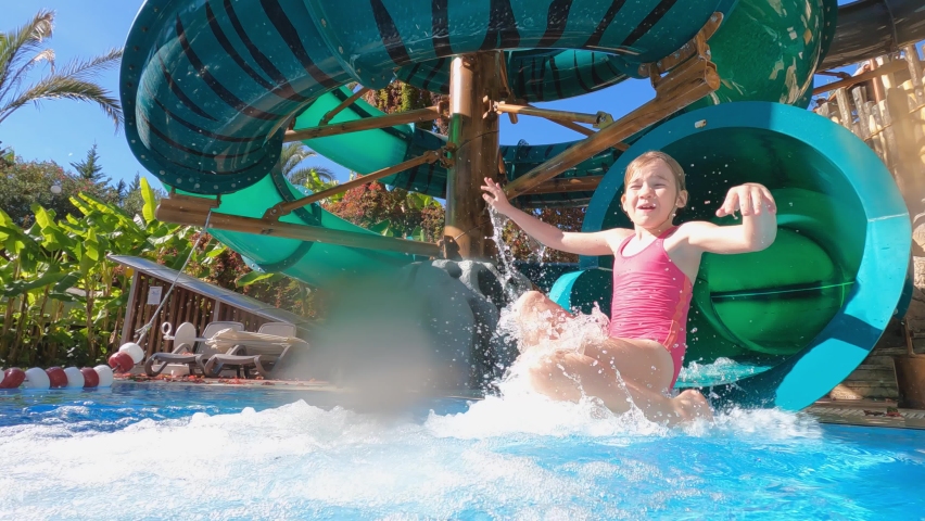 a little girl rolls down the slide to the pool in the water park. entertainment for children in the hotel by the sea. Royalty-Free Stock Footage #1082550403