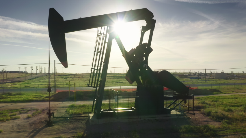 Pump jack working at oil well green field at summer. Oil production in California, USA. Beautiful silhouette shot of an oil pump, zoom in aerial 4K footage of raw fossil oil extraction business. 
