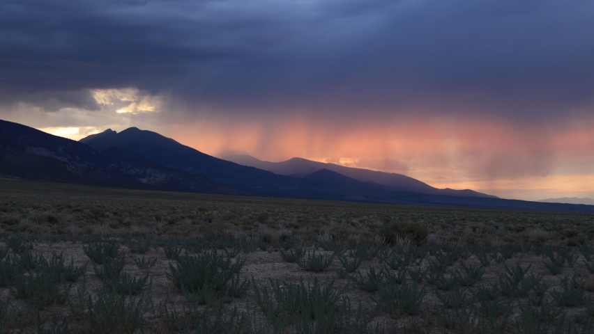 Orange light from the setting sun is filtered through rain clouds passing over the mountains in Great Basin National Park. As seen from Baker, Nevada on a summer evening.