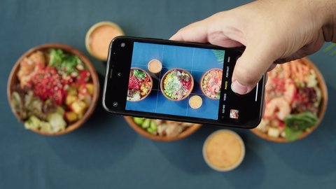 Taking photo of Hawaiian poke bowls, using smartphone top view. Cooked poke made of sliced vegetables, seafood and greenery. Healthy vegetarian dishes. Asian vegan raw meal, chopsticks.
