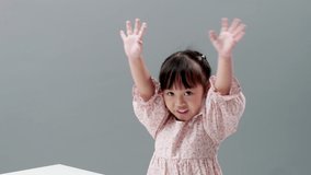 Little Asian girl wearing dress smiling, waving hands and looking at camera in studio. Concept of friendly asian kid.