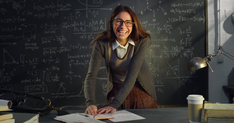 Cinematic shot of young female teacher is writing math formulas and equations on blackboard and explaining educational material task to her pupils or students in college or university classroom.
