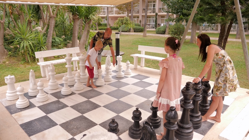 A big happy family with children plays giant chess in the park in the summer at the resort.