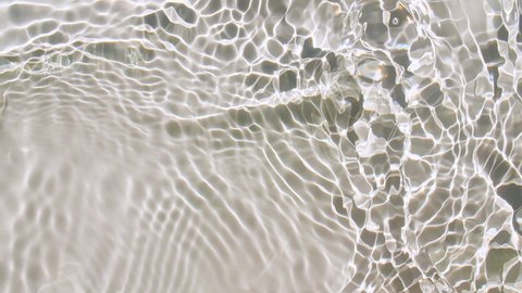 Pure beige water with reflections sunlight in slow motion. Water surface texture top view. Sun and shadows. Motion clean swimming pool ripples and wave.