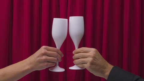Two hands with white champagne glasses making a cheers against red velvet background