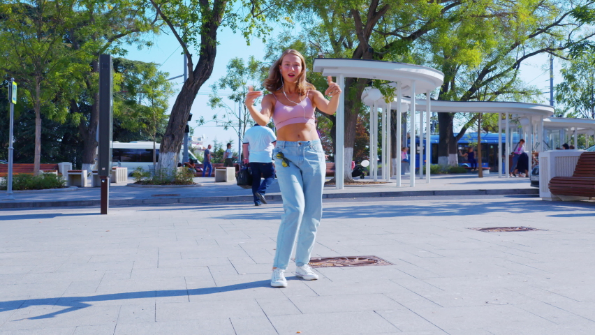 A woman in jeans clothes is dancing in the street. A young woman is dancing on the pavement at a sunny summer day