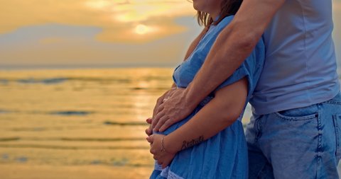 Close-up, a man carefully touches the tummy of his pregnant woman. Married couple expecting a baby, a man gently touches the tummy of a pregnant woman on the shore at sunset. Family values. 4k, ProRes