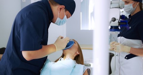 A male dentist performs a procedure for removing a cofferdam to a female patient in a modern dental office. High quality 4k video. Shot with RED camera.