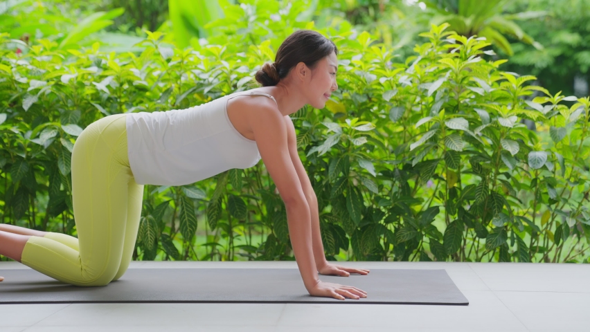 Young woman doing meditation exercise stretching sports, white tank top and yellow Legging, Female practicing yoga, natural balance between body and mental development. With bautiful green garden.