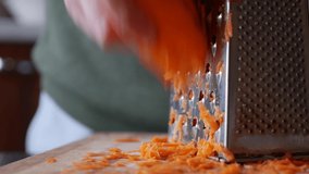 Close-up of a woman's hands grates carrots on a grater. Housewife grates carrot in kitchen.