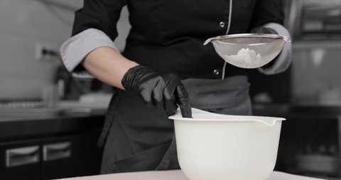 Pastry chef's hands in black gloves, sifting flour. The flour is sieved through a sieve. Cooking pizza, desserts, muffins, pies and other baked goods.