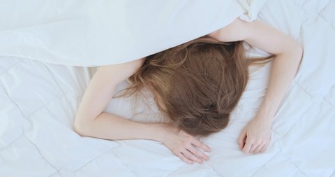 Young woman with beautiful fair skin sleeps on her stomach in her bed on white sheets. Woman tossing and turning in her sleep. Top view