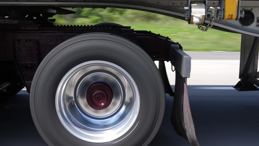 Driving beside commercial tractor trailer. Detail of burgundy wheels and trailer hitch. Highway driving in Ontario, Canada. Royalty-Free Stock Footage #1082600527