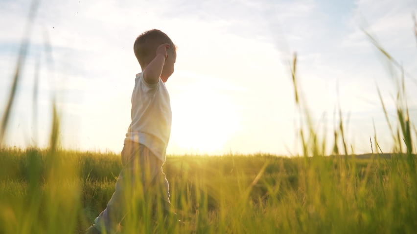 Happy kid walks on green grass. Child takes the first steps along rural road. Kid run in nature in park. Boy walks on grass in field. Happy childish dream concept in park. Boy run on green grass Royalty-Free Stock Footage #1082602033