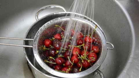 Ripe fresh cherries berry in steel sieve is hand washed under tap water in sink, top view
