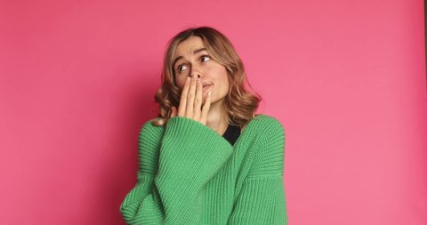 A bored woman wearing green dress is yawning isolated over pink background. Young sexy casual woman yawning, covering her mouth, rolling her eyes and feeling overly bored, is looking to the nails.