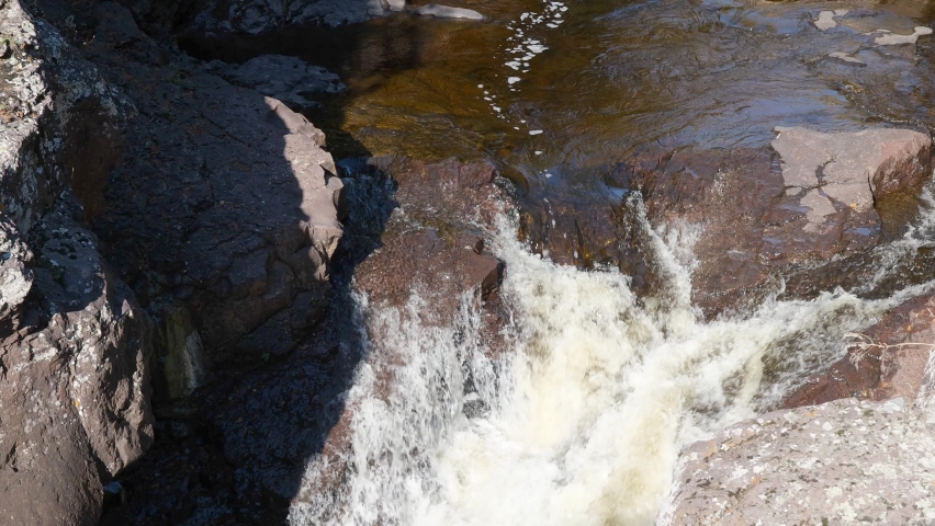 Closeup of water falls between rocks on the Temperance River in northern Minnesota, with zoom and tilt to include approaching river and rocky banks.