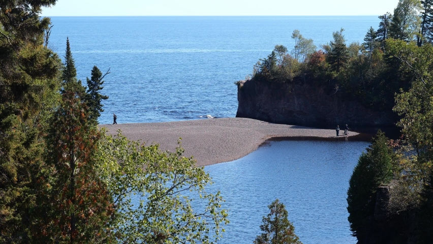 The mouth of the Baptism River where it enters Lake Superior in Minnesota, with a few people on the sandbar. At Tettegouche State Park on the north shore of one of the Great Lakes.