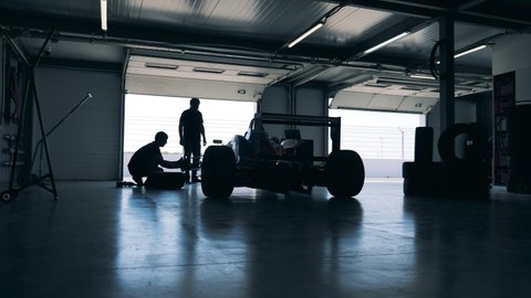 Servicemen are repairing a racing car in a garage