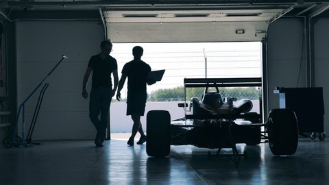 Owners of a racing car are observing it in the workshop