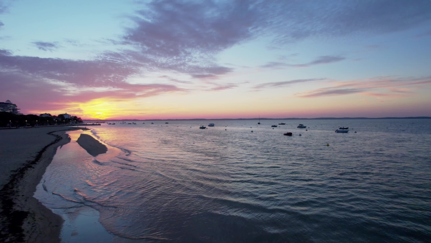 Aerial flyover ocea coast during colorful sunset, speed boats moored on harbor