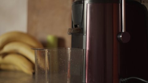 4K Centrifugal juicer pressing homemade carrot juice. Filing plastic cup with juice. Making freshly squeezed fruit and vegetable juice, close-up. Kitchen electrical appliances. Healthy drink, bananas
