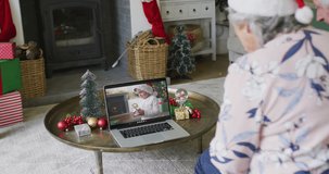 Caucasian senior woman with santa hat using laptop for christmas video call with boy on screen. christmas, festivity and communication technology.