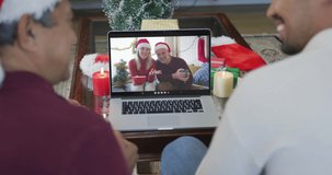 Biracial father and son with santa hats using laptop for christmas video call with couple on screen. christmas, festivity and communication technology.