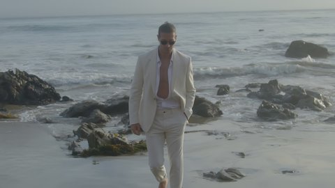 A young male model in a white suit by the ocean on the shore