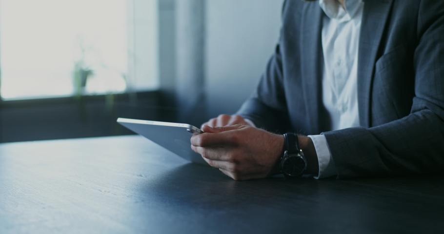 A man of European appearance, dressed in a business suit, uses a tablet while sitting at a table in the office, close-up Royalty-Free Stock Footage #1082625145