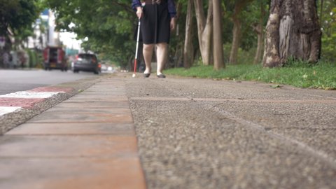 Defocused person with blindness visual disability blind woman walking on sidewalk with a long white cane a mobility tool used to detect objects in the path for blindness or vision impairment people.