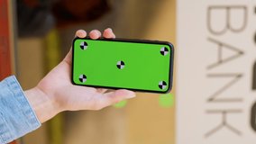 Woman using a smartphone green screen on blurred bank people background. Hands with a mobile phone, checking stock market data. Scrolling through, touching stock market graph on a touch screen device - Powered by Shutterstock - Get 15% off with code: PIKWIZARD15