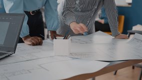 Close up of architects analyzing blueprints plans on table. Multi ethnic colleagues designing industrial sketch for building model and construction structure. Architectural layout. - Powered by Shutterstock - Get 15% off with code: PIKWIZARD15