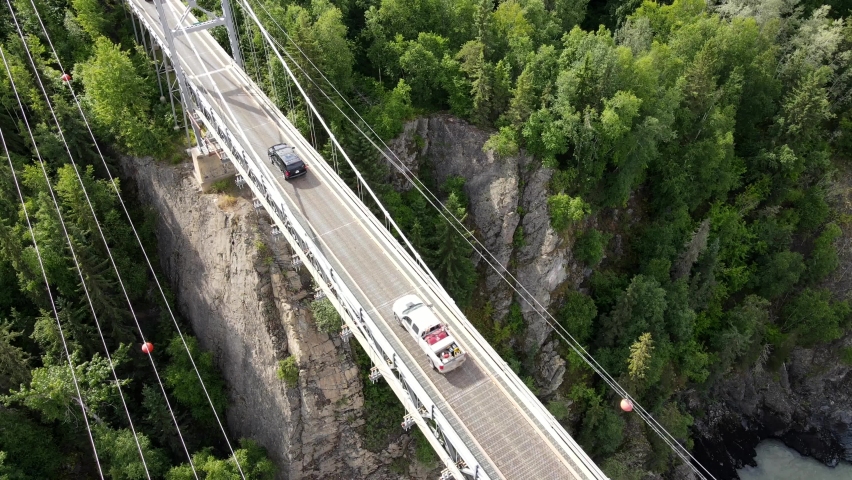 Rural landscapes of British Columbia. 4k aerial footage of canyon bridge with cars crossing it on a sunny day in northern Canada. Beautiful coniferous forest on steep slopes. Power lines underneath.