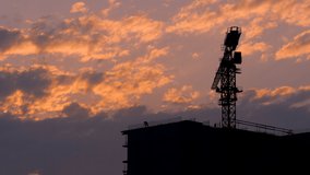 Work on the construction site of an apartment building. Construction of a residential complex. Silhouettes of a working crane and builders.