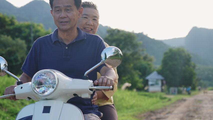 Happy asian elderly couple riding their vintage scooter enjoying a natural view, middle age lovers enjoying summer holiday vacation, motorbike rally activity, life insurance, family bonding care Royalty-Free Stock Footage #1082646637