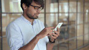 Young Indian business man using cellphone apps standing in office. professional businessman holding mobile phone managing finance banking applications corporate digital technology. - Powered by Shutterstock - Get 15% off with code: PIKWIZARD15