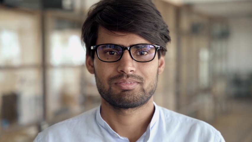 Headshot of young adult Indian businessman wearing glasses looking at camera posing in office. Sales manager, professional leader, company employee or entrepreneur close up portrait. Royalty-Free Stock Footage #1082651572