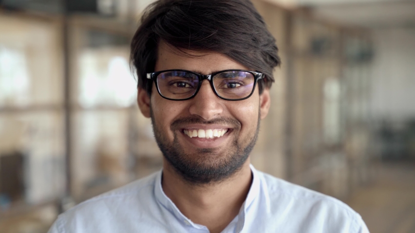 Headshot of young adult Indian businessman wearing glasses looking at camera posing in office. Sales manager, professional leader, company employee or entrepreneur close up portrait. | Shutterstock HD Video #1082651572