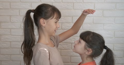 Girls measuring height. A young teen measure her height with her small sister in the room.