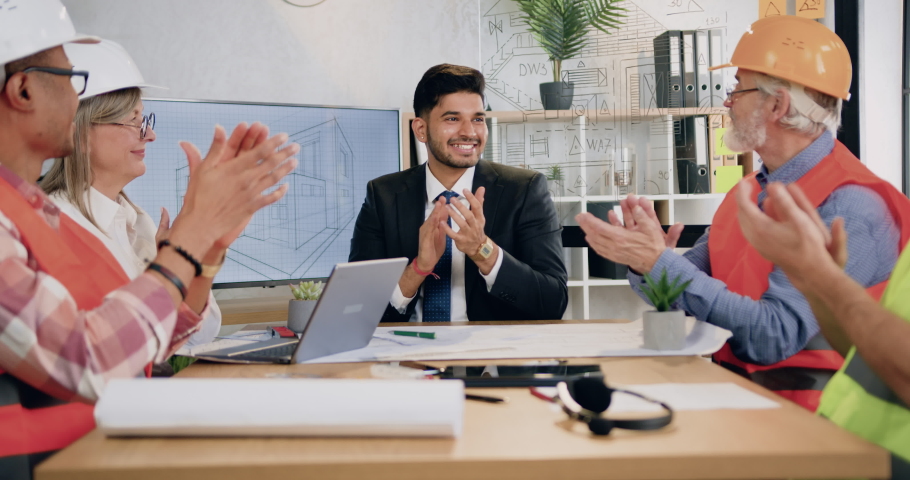 Success and luck concept where attractive satisfied high-skilled diverse male and female team of construction specialists applauding sucessful done architectural project in meeting room