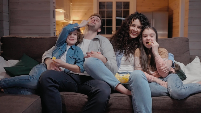 Family watching a movie together at home hugging, eating crisps and laughing. Family spends time together in lockdown. 50fps. High quality 4k footage
