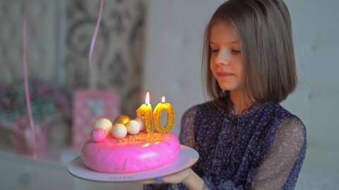 Cute happy young girl make a wish and blows out candles on birthday cake at party. The concept of a children's holiday. 10 years